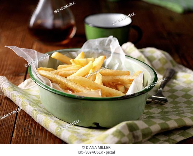 French fries in vintage bowl on tea towel, with vinegar bottle