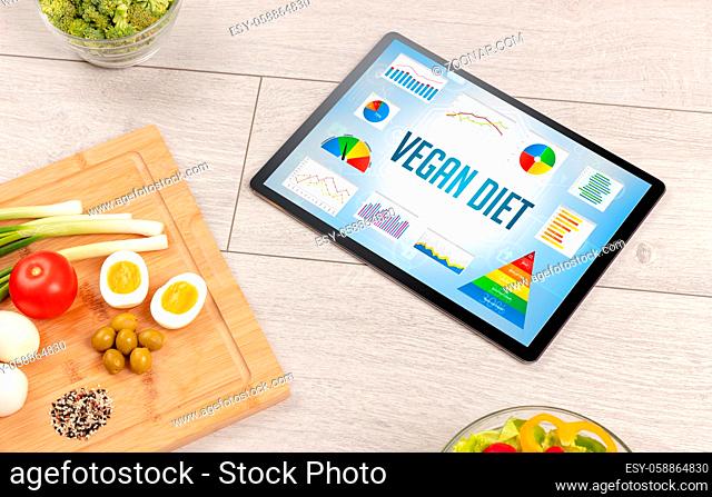 Organic food and tablet pc showing VEGAN DIET inscription, healthy nutrition composition