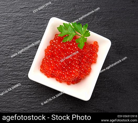 fresh grained red chum salmon caviar in a white ceramic bowl on a black slate stone background, top view