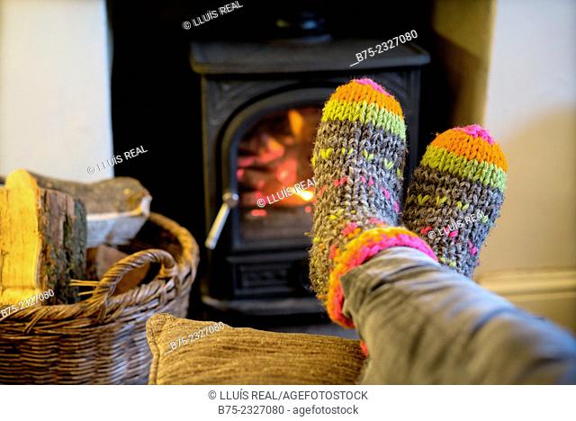 Feet warming up with a hand made colored socks in a position of rest and relax near a wood stove in winter