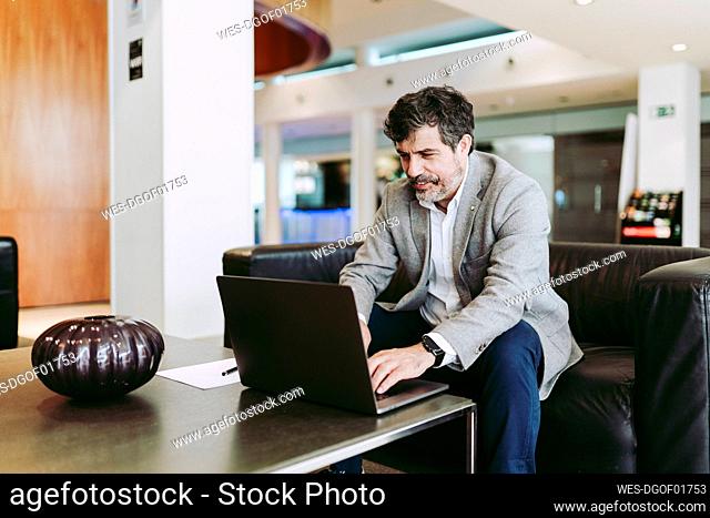 Male entrepreneur using laptop while sitting at lobby in hotel