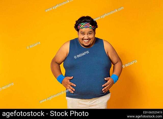 Portrait of a fat man smiling while placing hands on belly against plain background