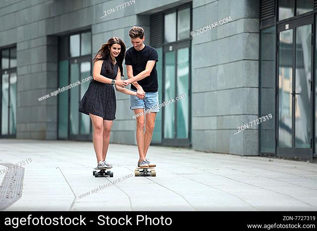 Young pair in love of stylish teenagers ride longboards tenderly holding hands on in the industrial background