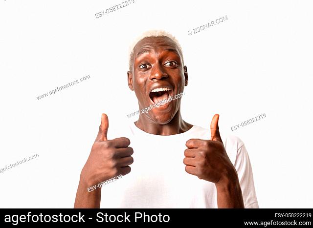 Portrait of cheerful and excited handsome african-american blond guy looking with rejoice, showing thumbs-up and smiling, approve or recommend something