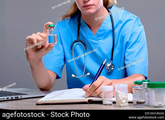 Caucasian female doctor holding vaccine vial, isolated on grey background