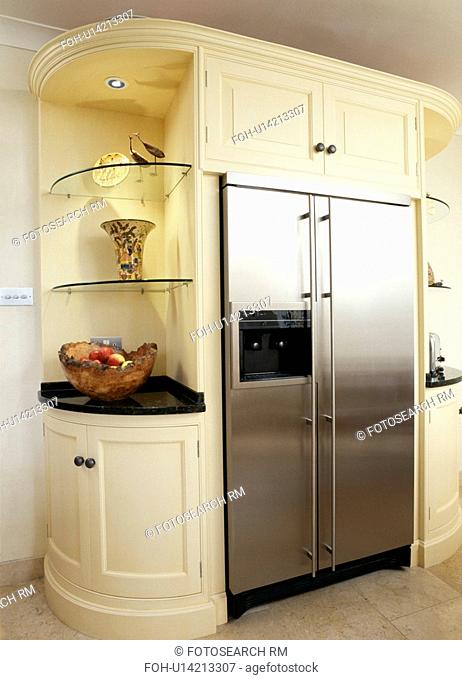 Stainless-steel American-style fridge freezer built into cream kitchen unit with glass corner shelves