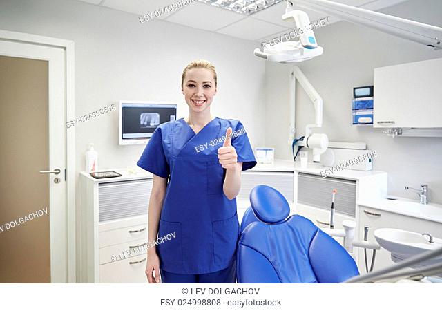 people, medicine, stomatology and healthcare concept - happy young female dentist showing thumbs up at dental clinic office