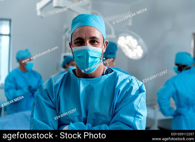 Portrait of caucasian male surgeon wearing face mask and protective clothing in operating theatre