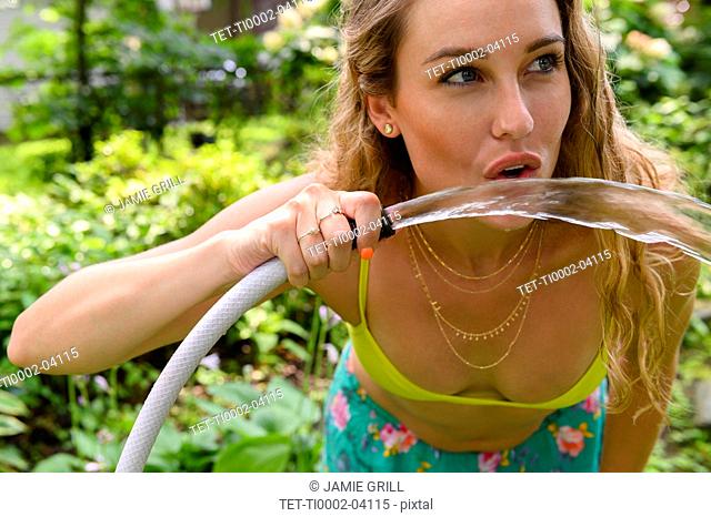 Young woman drinking from garden hose