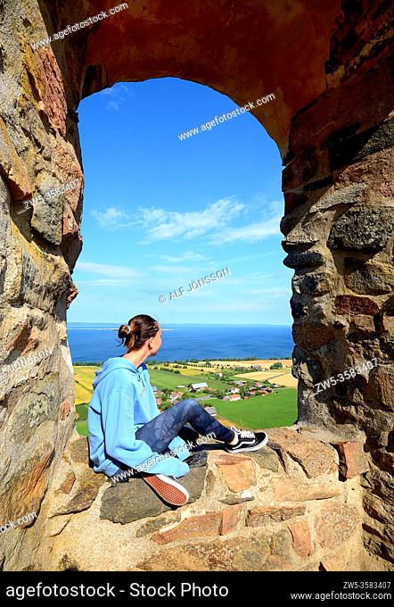 Girl sitting in a window in Brahehus Castle ruin, which is situated outside Graenna in Joenkoeping County in the province of Smaland, Sweden