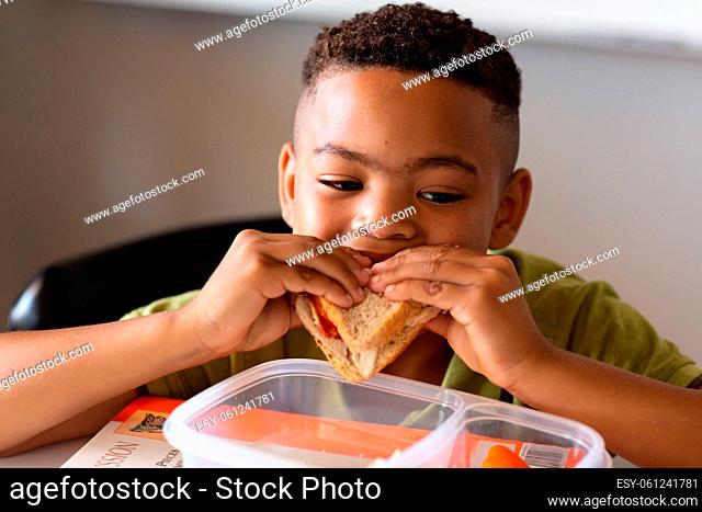 Close-up of african american elementary schoolboy eating sandwich at desk during lunch break