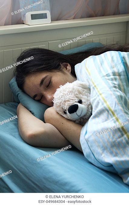 The young girl has a cold, lies in bed at home, feels unwell, takes medicines and vitamins, sleeps with a toy bear