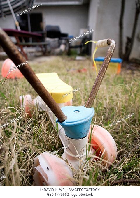 Childrens tricycle abandoned in the grass of a foreclosed home in Fresno, California, United States