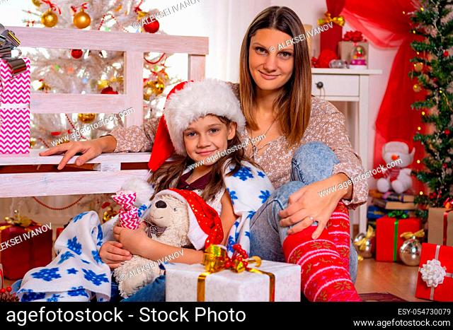 Beautiful mom and daughter sit on the floor in the Christmas interior and smile in the frame