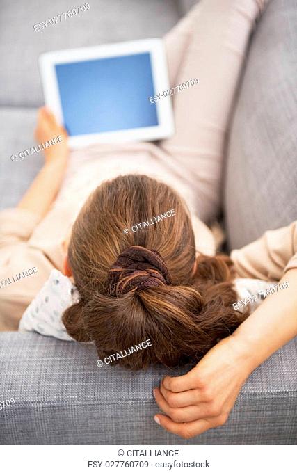 Young woman laying on sofa with tablet pc . rear view