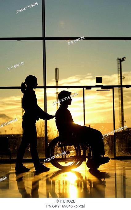 Silhouette of a woman pushing a male patient sitting in a wheelchair