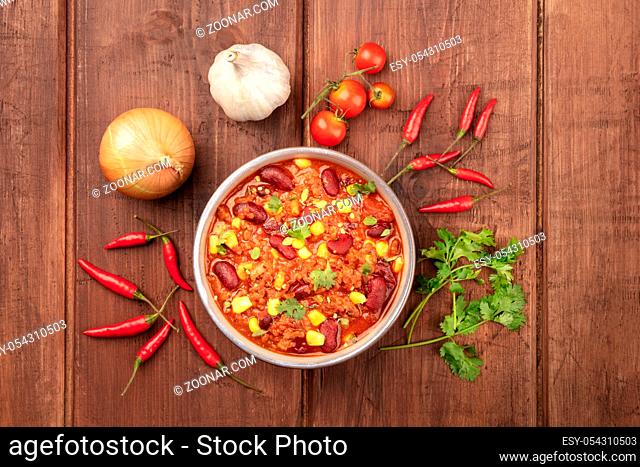 Chili con carne, shot from the top on a dark rustic wooden background with ingredients