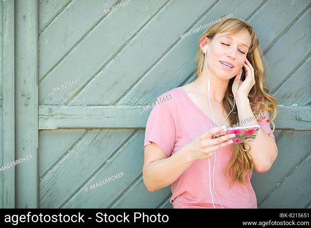 Outdoor portrait of young adult brown eyed woman listening to music with earphones on her smart phone