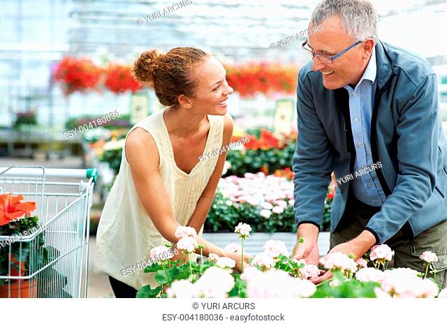Ethnic young woman standing next to male florist bending down looking at flowers smiling at each other