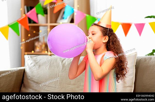 little girl in birthday party hat blowing balloon