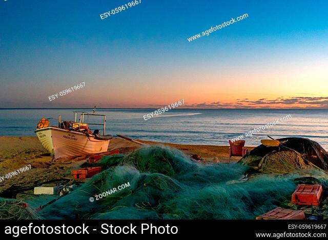 Amarcao da Pera, Portugal - 30 December 2020: sunset at the Praia do Pescadores on the Algarve coast of Portugal with fishing boat and nets