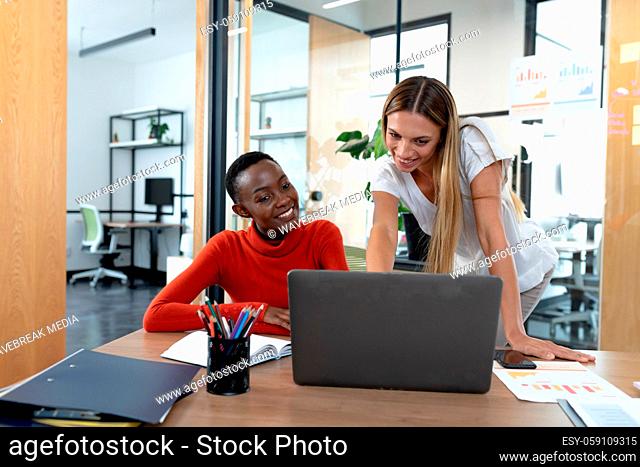 Diverse female business colleagues looking at laptop computer and smiling in meeting room