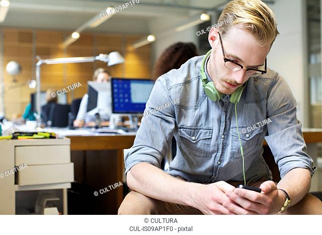 Young man choosing music from smartphone in office