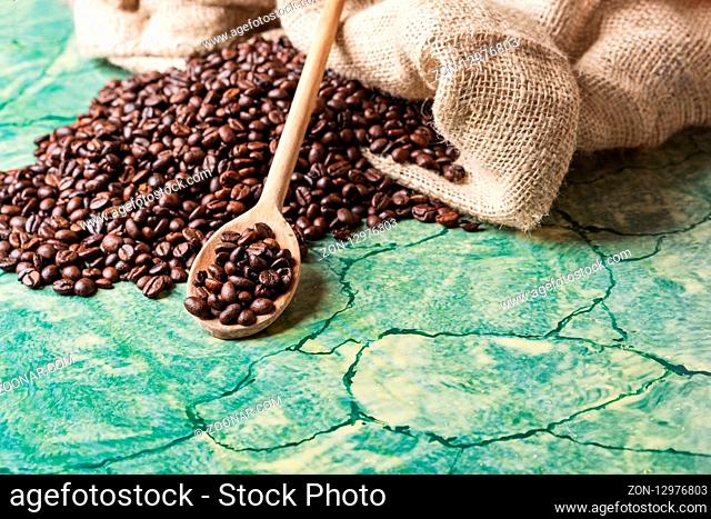 Coffee beans in coffee burlap bag on green table and wooden spoon with coffee beans on top