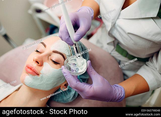 Young woman applying mask of clay on face in beauty spa