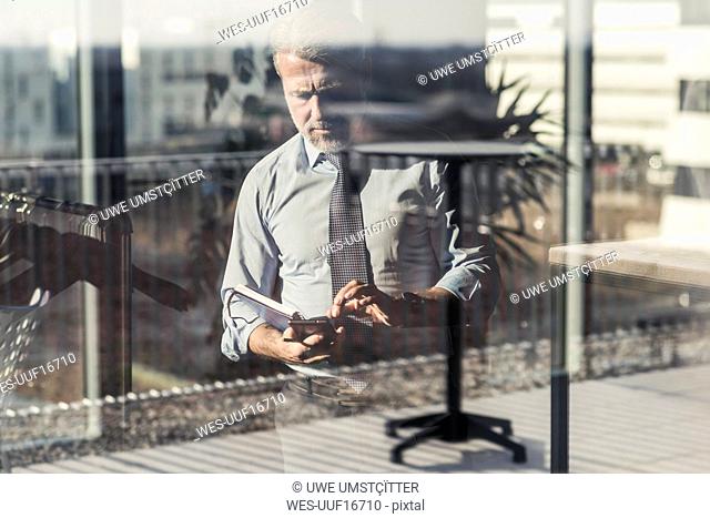 Mature businessman using cell phone behind windowpane