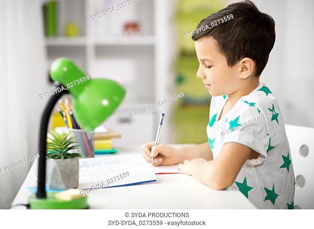 boy with book writing to notebook at home