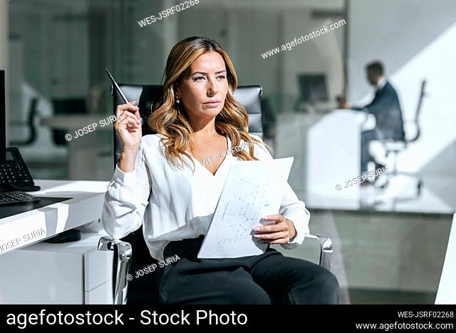 Thoughtful businesswoman sitting with document in office