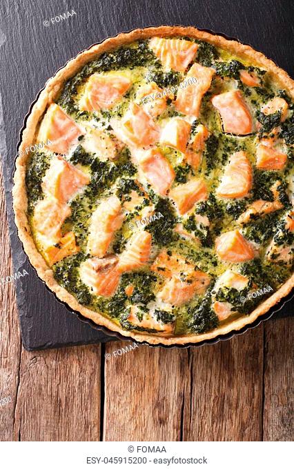 pie with salmon, cream and spinach in baking dish close up on a table. vertical view from above