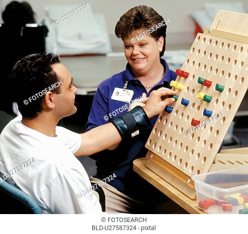 Man with a disability putting pegs in a board during a session with his occupational therapist
