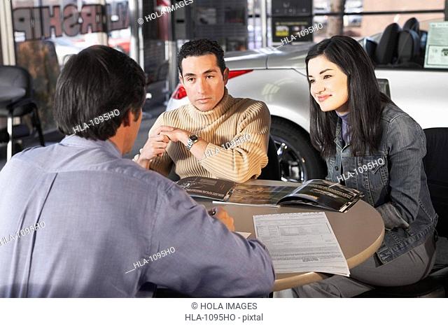 Rear view of a salesman talking to a couple in a car showroom