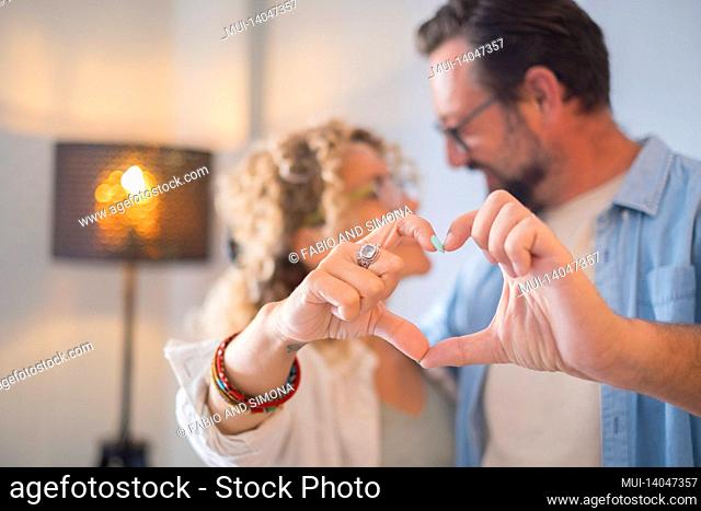 happy adult couple in love do heart sign with hands - relationship people enjoy home together - concept of man and woman married and joyful for new apartment -...