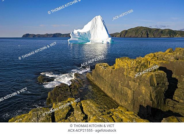 Iceberg floats in Trinity Bay off the rocky shoreline of Bonavista Peninsula in eastern Newfoundland, Newfoundland and Labrador, Canada