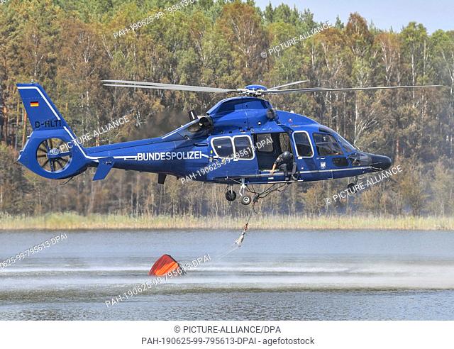 25 June 2019, Brandenburg, Lieberose: A helicopter of the federal police picks up water in the tar furnace lake to fight the forest fire in the Lieberoser Heide