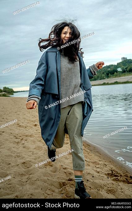 Happy woman wearing blue raincoat running at shore