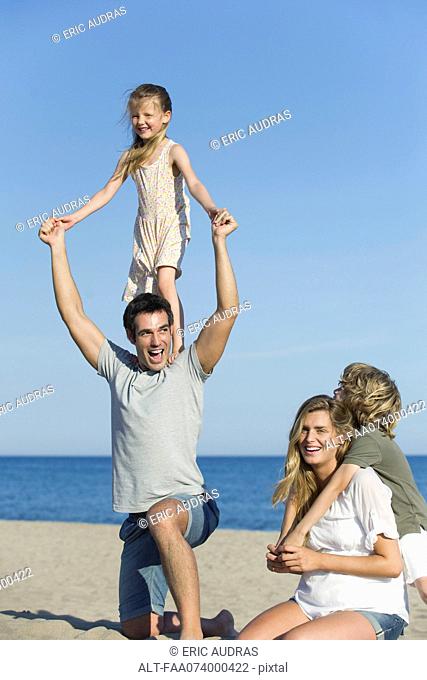 Family playing together at the beach, girl standing on her father's shoulders