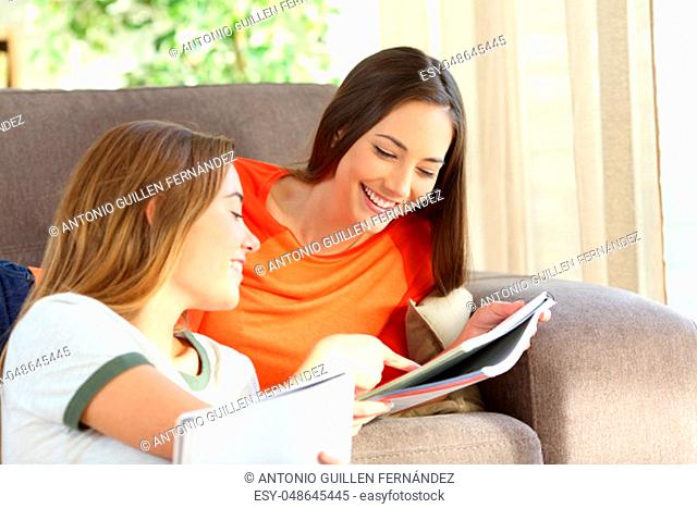 Students studying and helping each other with notebooks on a sofa in the living room at home