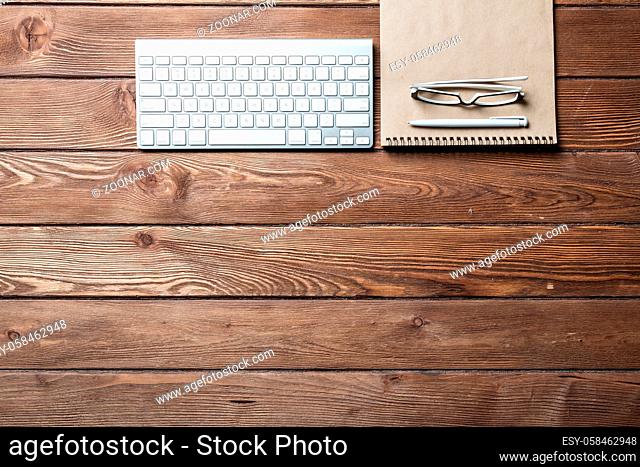 Top view of modern businessman workplace. Spiral notepad and computer keyboard on brown wooden surface. Education, creativity and innovation concept with copy...