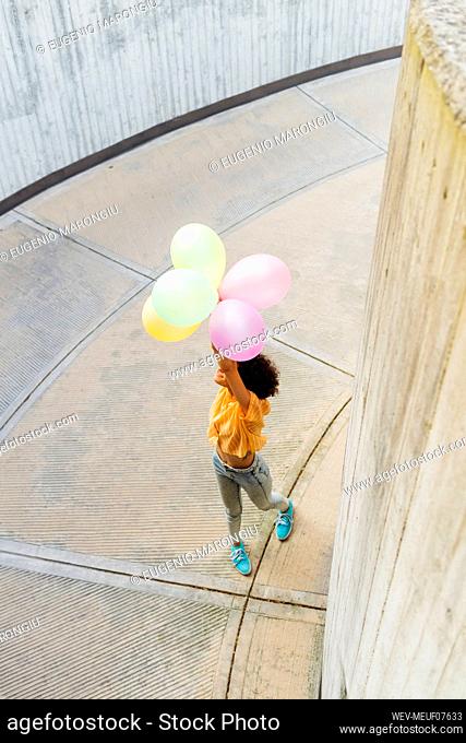 Playful woman holding balloons standing on footpath