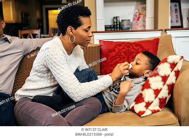 Black woman wiping nose of son on sofa