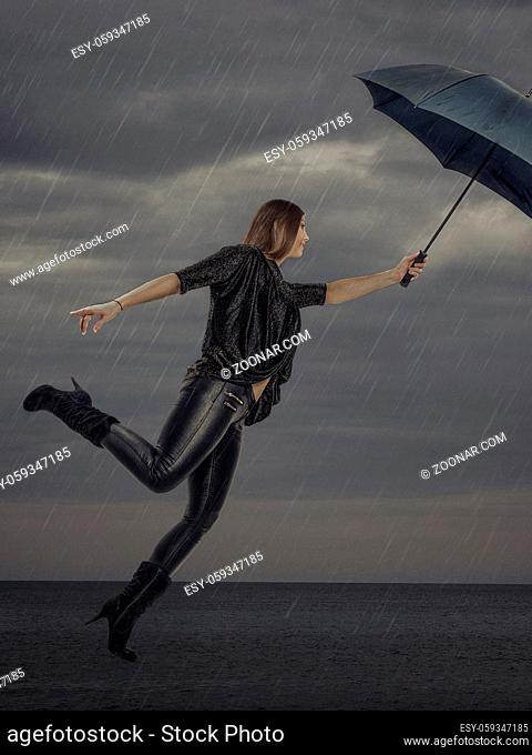 Junge Frau mit Regenschirm fliegt mit ihrem Schirm stetig nach oben