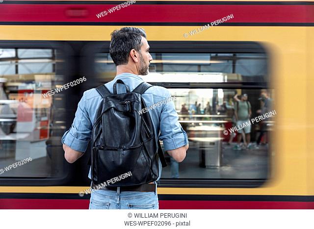 Rear view of man with backpack at the station platform while train coming in