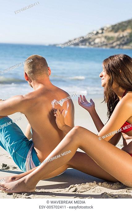 Smiling woman drawing heart pattern with sun cream on her boyfriends back