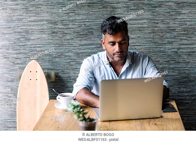 Casual businessman with skateboard using laptop in a cafe