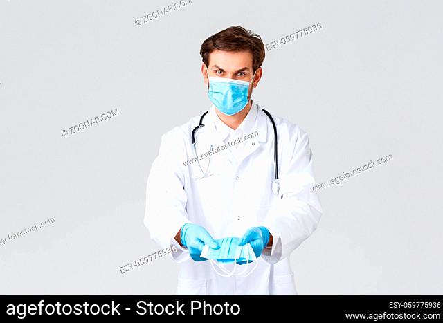 Hospital, healthcare workers, covid-19 treatment concept. Serious thoughtful doctor in scrubs and gloves, giving medical masks for patient protection during...