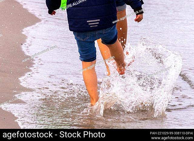 29 October 2022, Mecklenburg-Western Pomerania, Boltenhagen: Children are barefoot during a walk on the beach at the Baltic Sea coast and splash with water